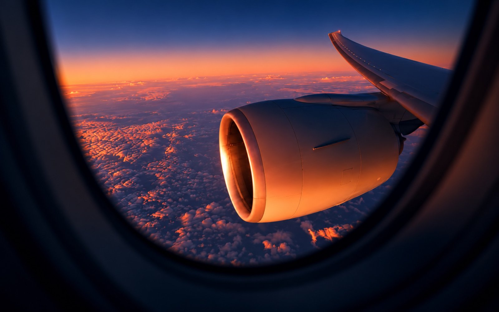 Jet engine seen through a cabin window above the clouds at sunset